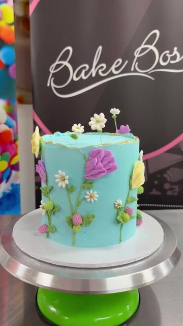 Turquoise buttercream cake decorated with colorful sugar flowers on a cake stand