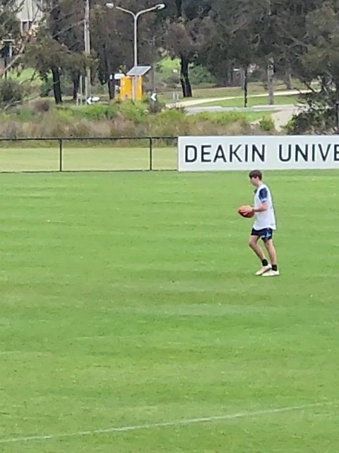Person holding a football on a wide grass field at a university sports ground.
